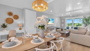 A modern dining area with a wooden table set for six, white chairs, and a central floral arrangement.