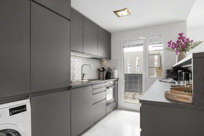 A modern kitchen with grey cabinets, a built-in oven, and a coffee machine.