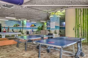 Zona recreativa con mesas de ping pong, billar y un mural que representa una playa.
