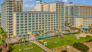 Ein mehrstöckiges Hotel mit Poolbereich, Liegestühlen und einem gepflegten Rasen.