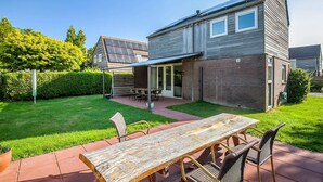 Een modern huis met een terras, een eettafel en stoelen.