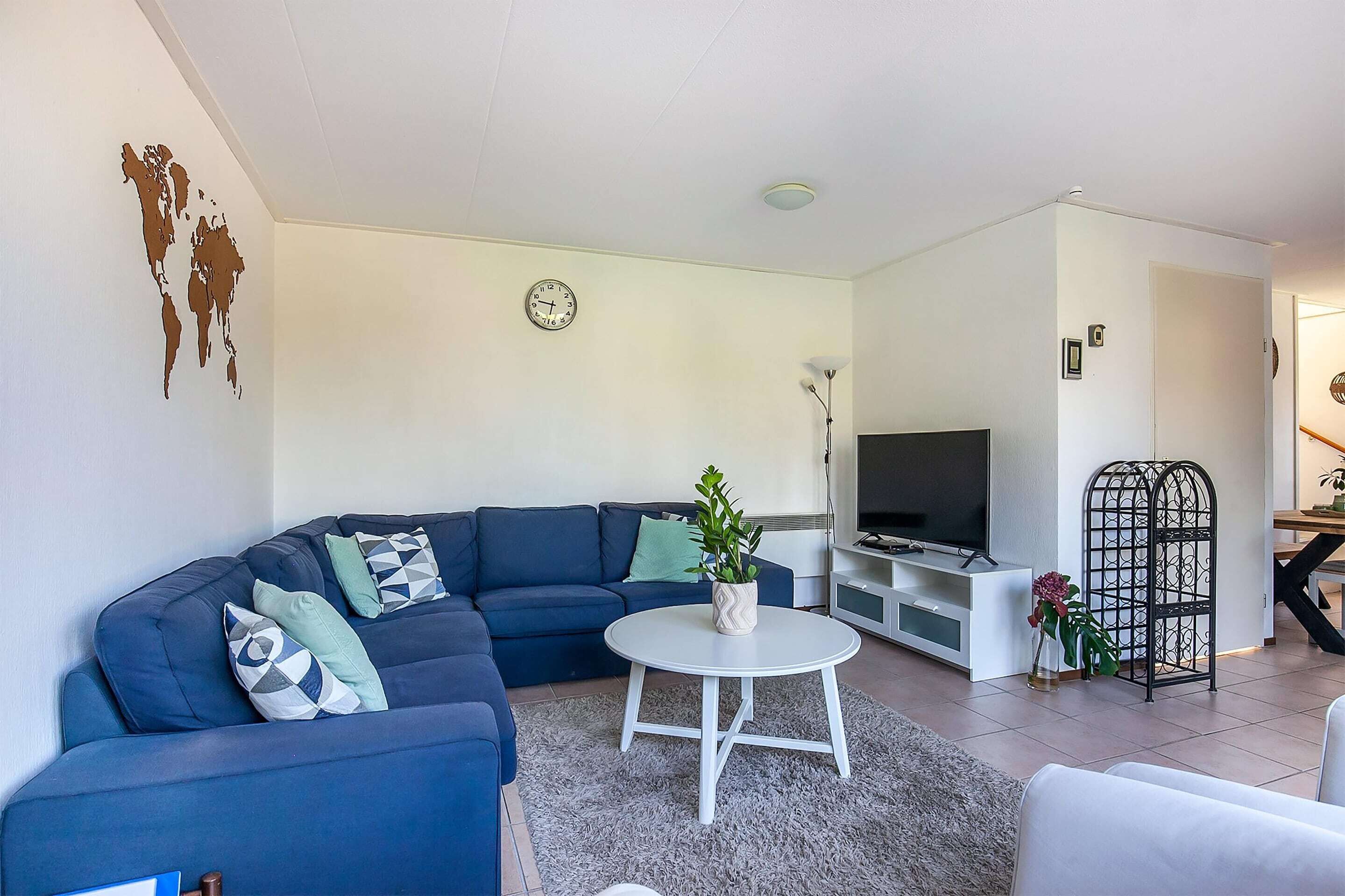 A modern living room with a sectional sofa, a white coffee table, a flat-screen TV, and a decorative plant.