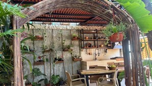 A rustic outdoor dining area with a wooden pergola, potted plants, and a stone wall backdrop.