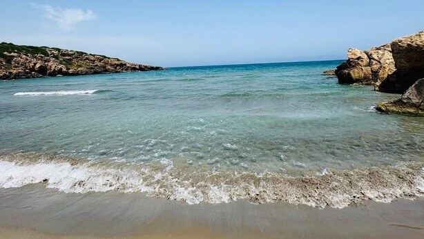 Une plage à l’eau claire, bordée de formations rocheuses et d’un rivage sablonneux.