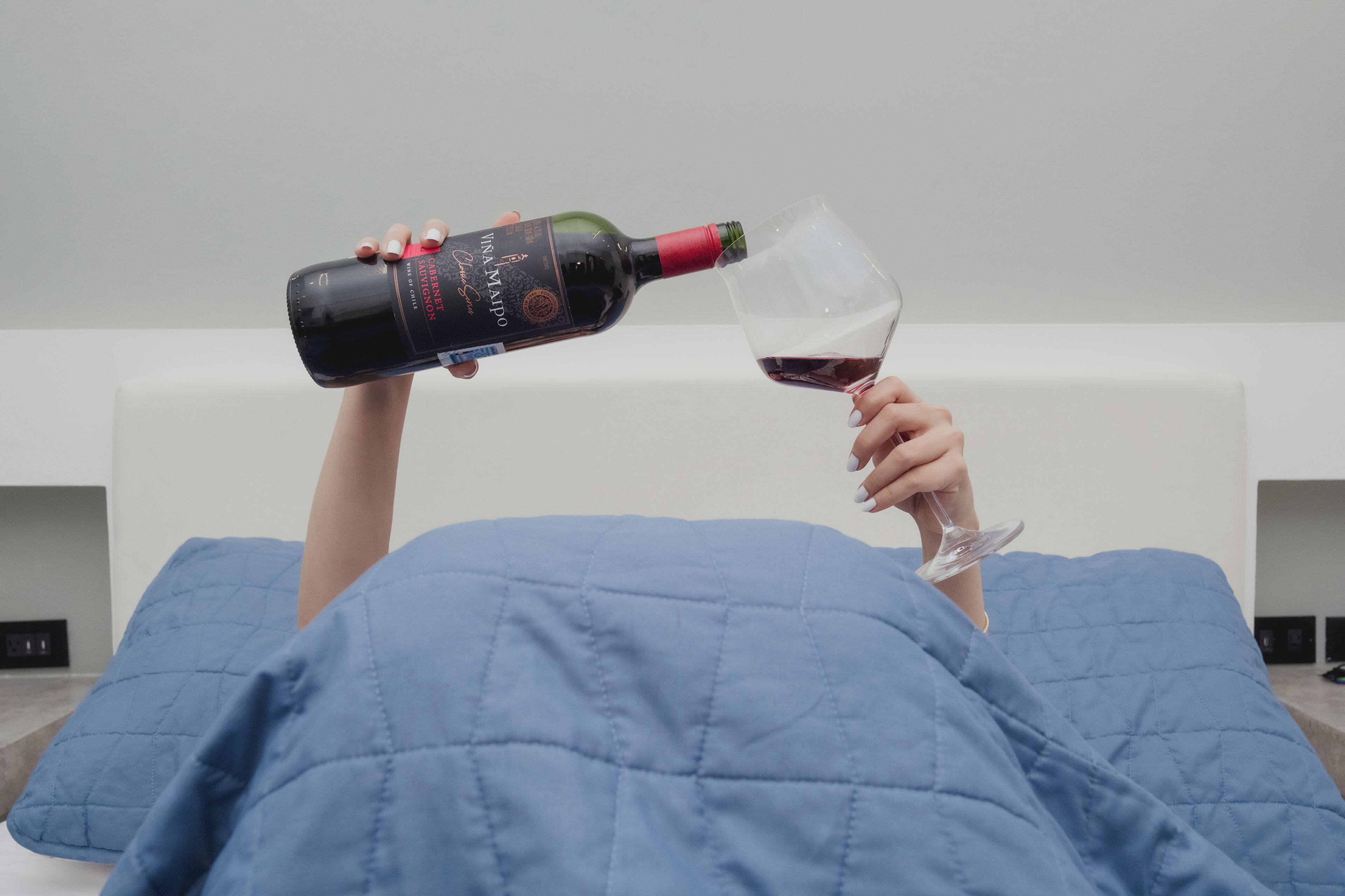 Una persona acostada en la cama con una botella de vino y una copa.