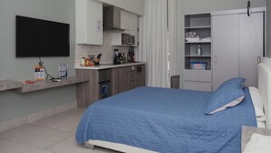 A modern hotel room with a bed, a kitchenette, a flat-screen TV, and a wardrobe. - Apartamento Santa Rita #5 cerca de restaurantes (Danlí)