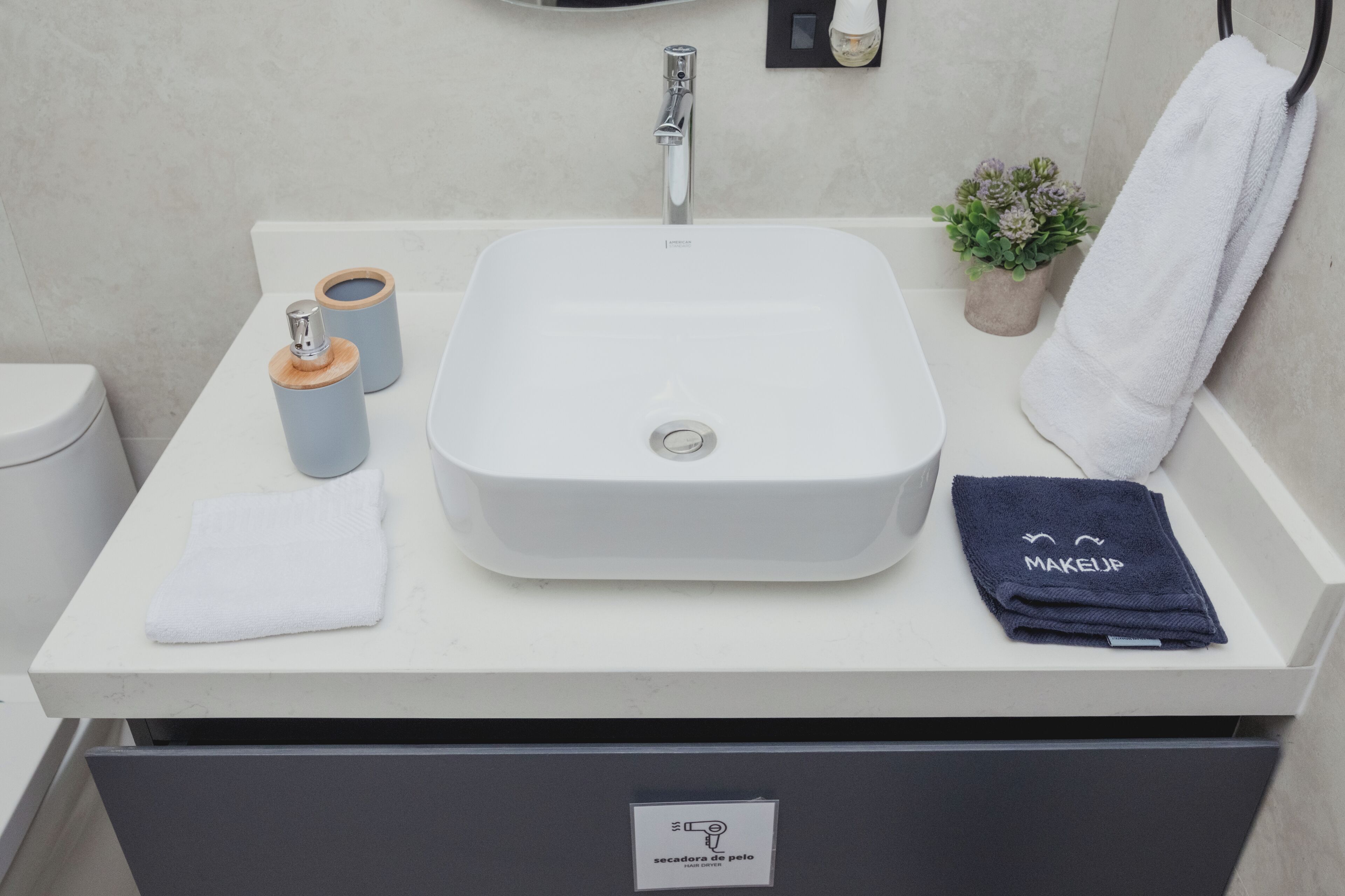 A bathroom with a white sink, a towel, a makeup towel, and a small potted plant.