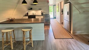 A modern kitchen with a central island, wooden flooring, and pendant lighting.