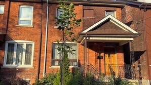 A two-story brick building with a front porch, a small tree, and a well-maintained lawn.