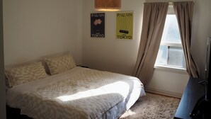 A bedroom with a bed, a hanging light fixture, two posters on the wall, and a window with curtains.