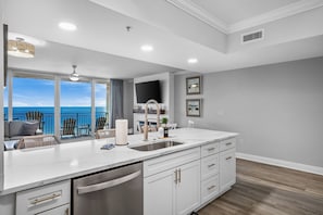 A modern kitchen with a large window overlooking the ocean, a built-in oven, and a stainless steel dishwasher.