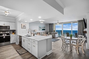 A modern kitchen with a central island, a dining area with a view, and a living room with a sofa and artwork.