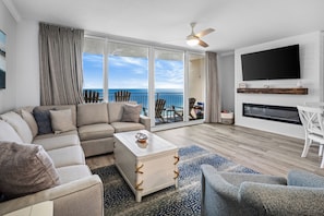 A modern living room with a sectional sofa, a coffee table, and a flat-screen TV mounted on the wall.