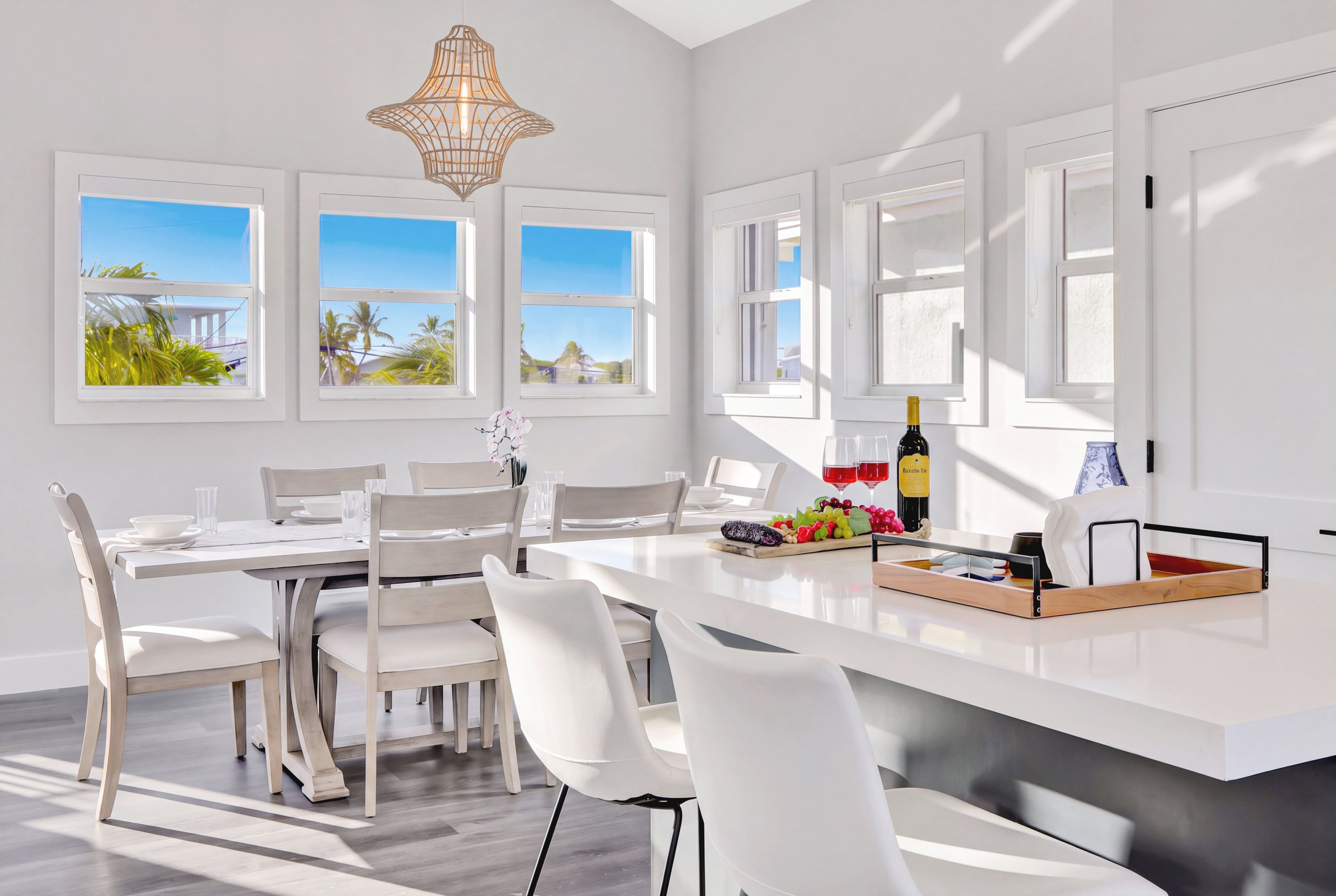 A modern dining area with a white table, chairs, and a central island with a bottle and glasses.