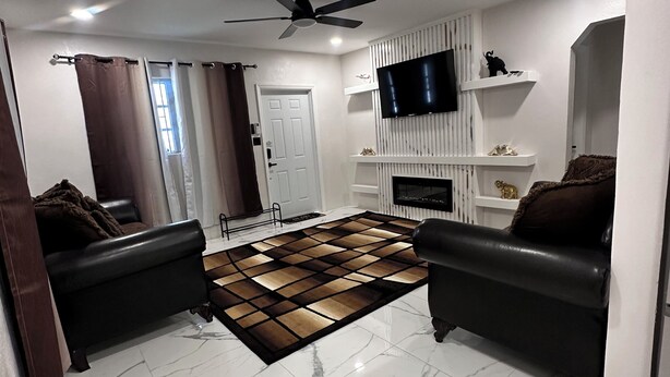 A modern living room with a fireplace, two black leather sofas, a patterned rug, and a flat-screen TV mounted on a white wall.