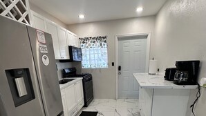 A compact kitchen with white cabinets, a stainless steel refrigerator, a stove, and a coffee maker.