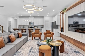 Una sala de estar moderna con un sofá, sillas, una mesa de centro y una cocina al fondo.