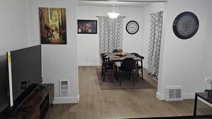 Un salon avec un téléviseur, un coin repas avec une table et des chaises, et une cuisine équipée d’une cuisinière.