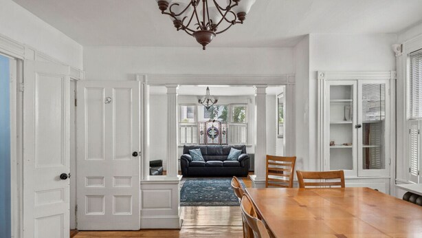 A spacious dining area with a wooden table and chairs, a dark-colored sofa with a blue cushion, and a chandelier.
