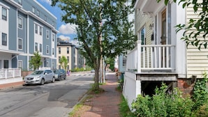 A residential street with houses, a sidewalk, and parked cars.