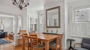 A dining area with a wooden table and chairs, a chandelier, and a large mirror on the wall.