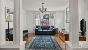 A spacious living room with a dark leather sofa, a blue patterned rug, and a chandelier.