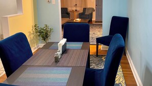 Un coin repas avec une table dressée pour quatre personnes, entourée de chaises bleues, donnant sur un salon par le biais d’une arche.