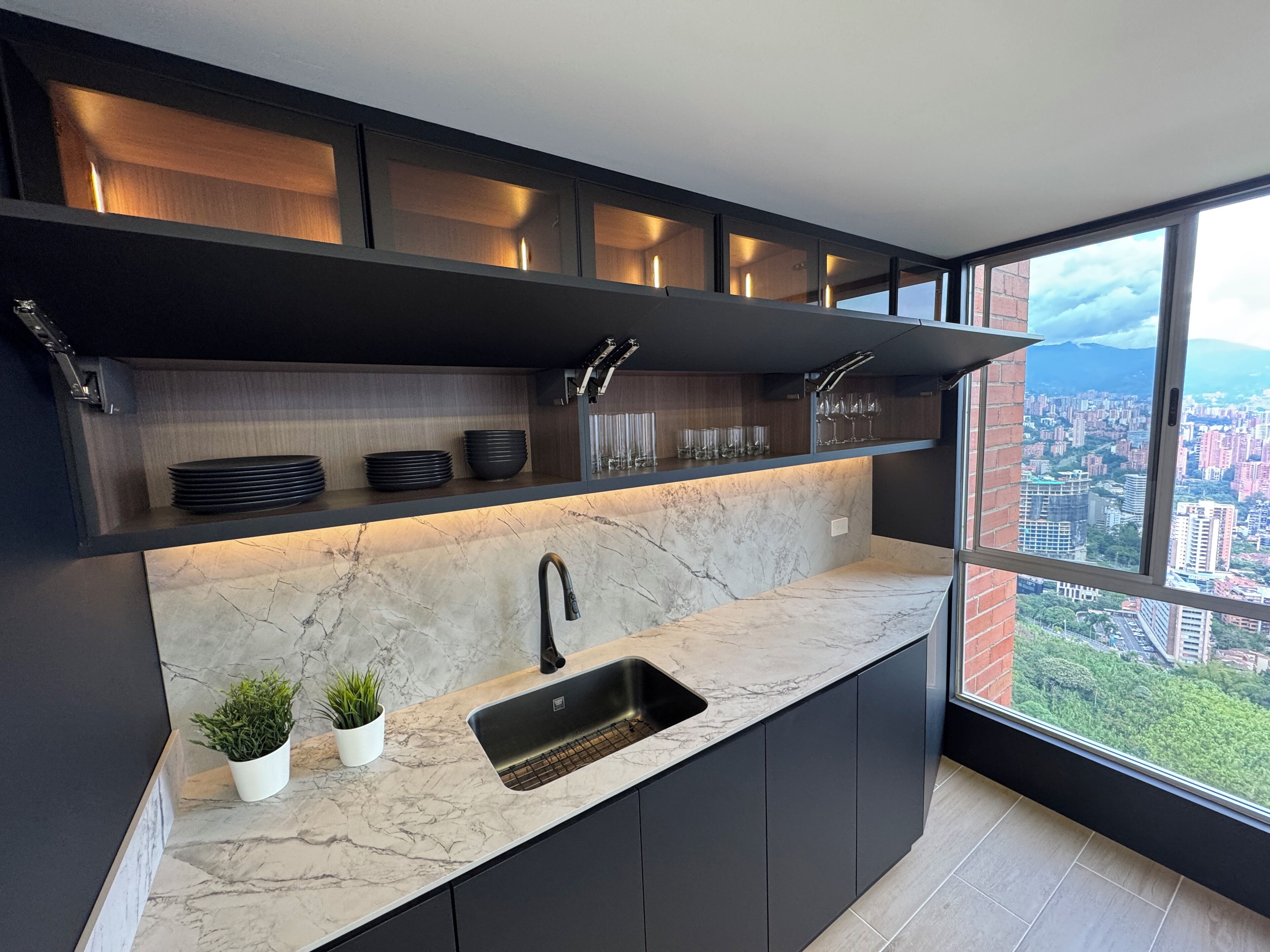 Eine moderne Küche mit integriertem Spülbecken, dunklen Schränken und Blick auf eine Stadtlandschaft durch große Fenster.