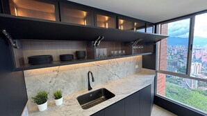 Una cocina moderna con un lavamanos integrado, muebles oscuros y vistas a un paisaje urbano a través de amplios ventanales.