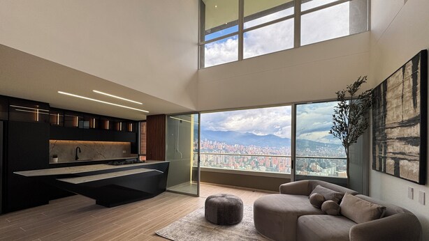 Una sala de estar moderna con un ventanal grande, un sofá, una mesa de centro y una zona de cocina con encimera y armarios.