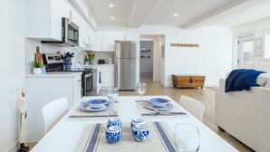 Una cocina moderna con armarios blancos, un refrigerador de acero inoxidable y un comedor con una mesa blanca dispuesta para dos.