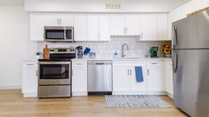 Una cocina moderna con armarios blancos, electrodomésticos de acero inoxidable y un cartel que dice 'RELAX'.