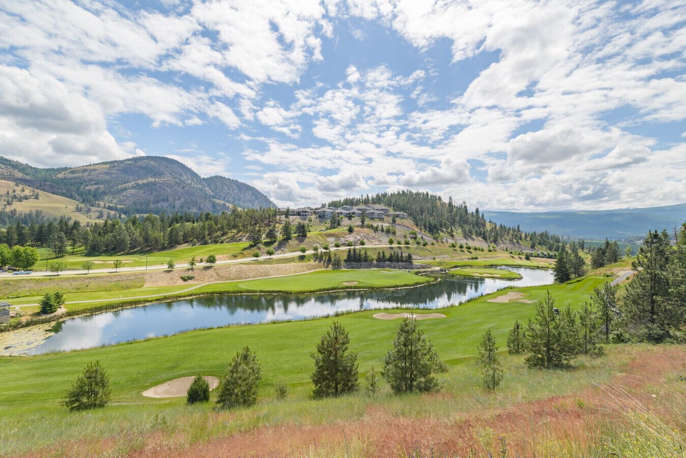 A golf course with a pond, surrounded by trees and hills.