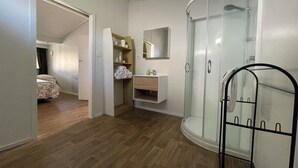Een slaapkamer met een houten vloer, een kledingkast met planken, een badkamer met een douchecabine van glas en een bed met een bloemenprint sprei.