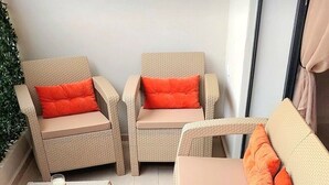 Un coin salon extérieur en osier, composé de deux canapés et de deux fauteuils, chacun agrémenté de coussins orange. On y trouve une petite table sur laquelle sont posées trois bougies blanches et un verre.
