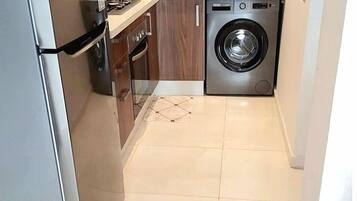 A compact kitchen with a stainless steel refrigerator, a washing machine, and a sink.