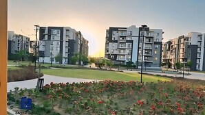 Zona residencial con edificios de apartamentos modernos, un parque con césped y un letrero azul con texto.