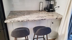 Eine Küche mit weißen Schränken, einer Granit-Arbeitsplatte, einer Kaffeemaschine und zwei Barhocker.