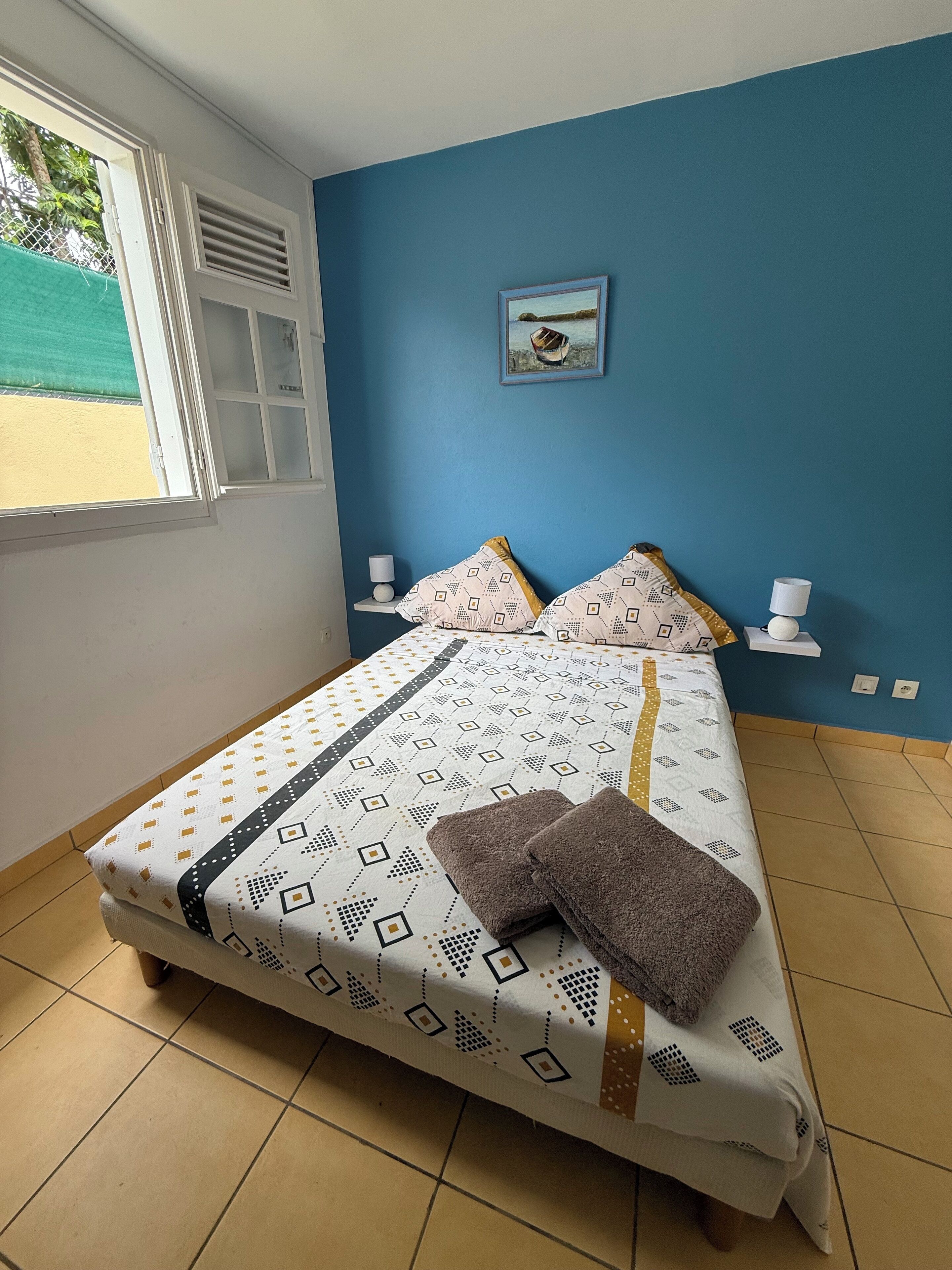 A bedroom with a bed, pillows, a nightstand, a window, and a wall-mounted picture.