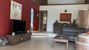 A spacious living area with a high ceiling, wooden beams, a television, a sofa, a coffee table, and a doormat with "Bienvenue & Chalandais" text. - Between sun and river: your perfect getaway (Goyave)