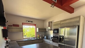 A modern kitchen with a large island, stainless steel appliances, and a red accent wall. - Between sun and river: your perfect getaway (Goyave)