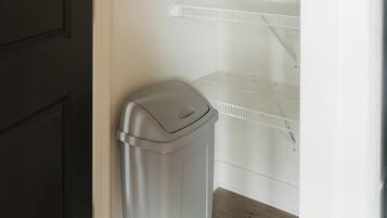 A laundry room with a trash bin and white shelving units.