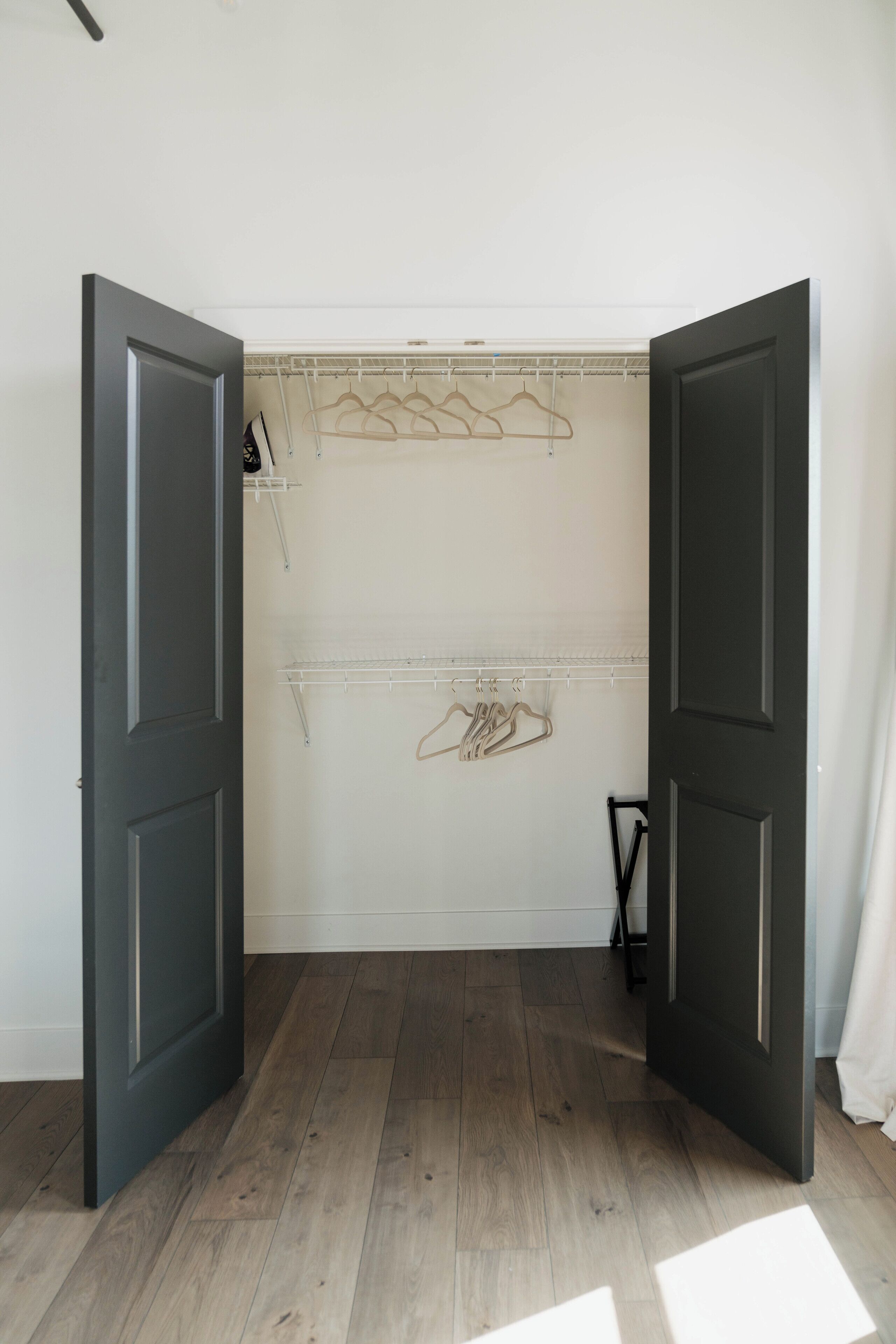 A room with a wooden floor, a closet with hanging clothes, and a door.