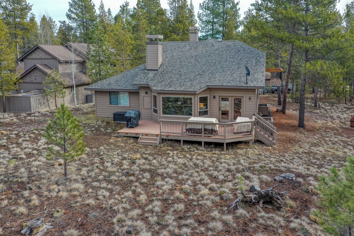 A two-story house with a deck, surrounded by trees and a dry grassy area.