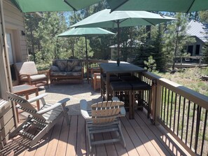 A wooden deck with outdoor furniture, including chairs and a table, under green umbrellas. - Super clean, quiet and comfy 3/2. (Sunriver)