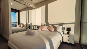 Un dormitorio moderno de hotel con una cama grande, una mesita de noche, un espejo y una ventana con vistas.