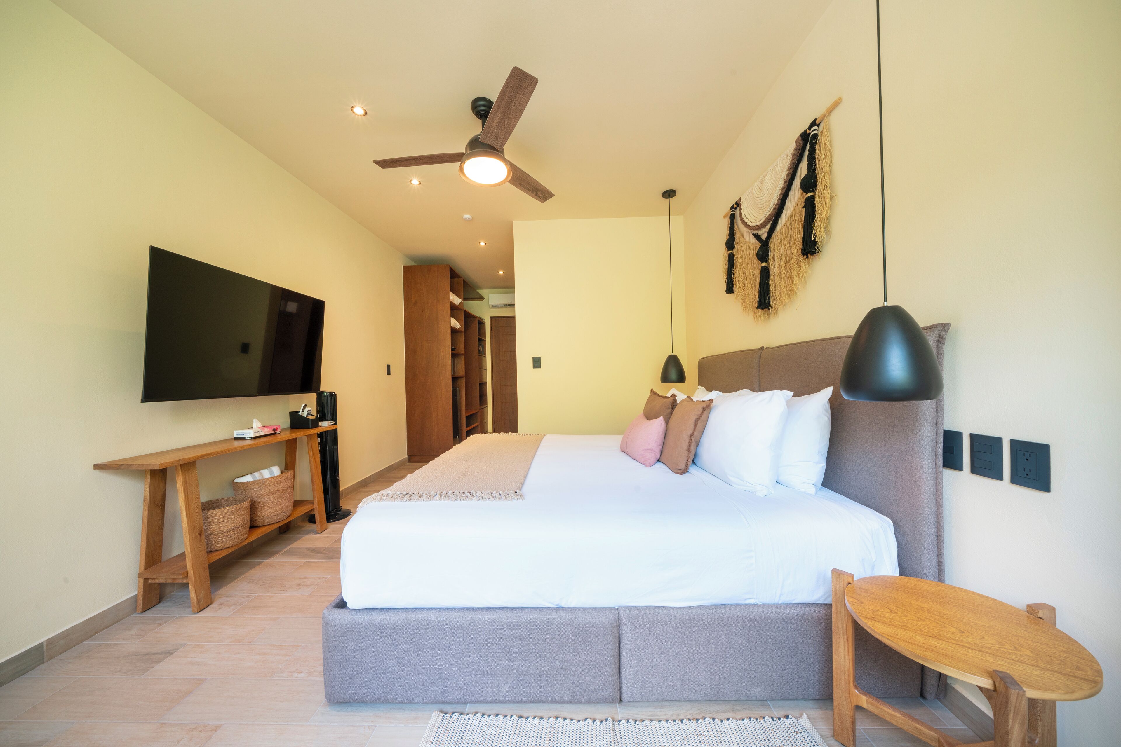 A modern bedroom with a large bed, a TV, a ceiling fan, and a wooden side table.