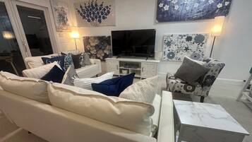 Una sala de estar con un sofá blanco, un sillón estampado, un televisor y decoración en la pared.