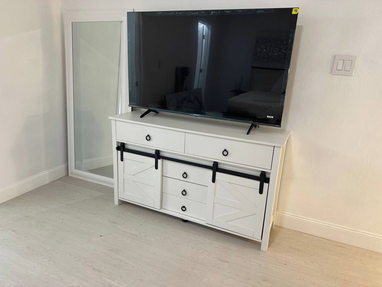 Un mueble blanco de entretenimiento con televisor de pantalla plana, cajones y puerta corredera.