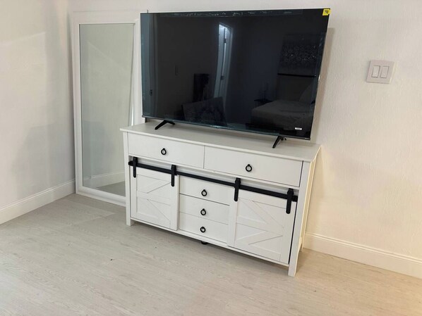 A white entertainment unit with a flat-screen TV, drawers, and a sliding door.
